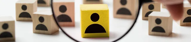 Lupe vor einigen Holzklötzen mit Personen-Icons Lupe vor einigen Holzklötzen mit Personen-Icons